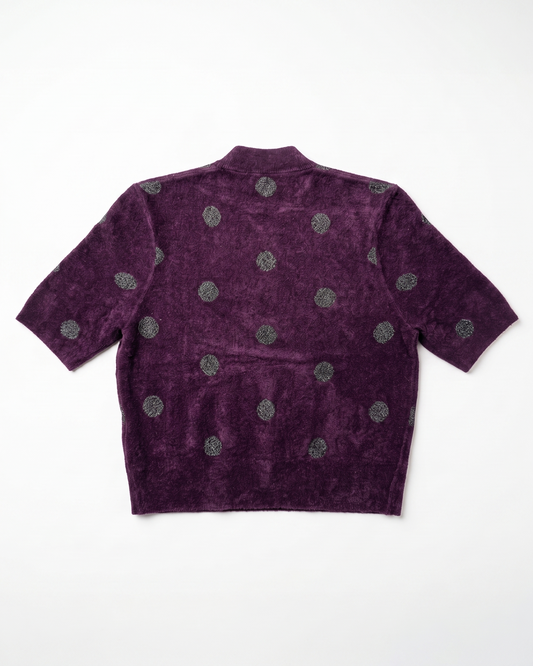 A short-sleeve cropped knit top in deep purple with a textured, velour-like finish, featuring a pattern of metallic silver-gray circular medallions, shown flat against a white background.