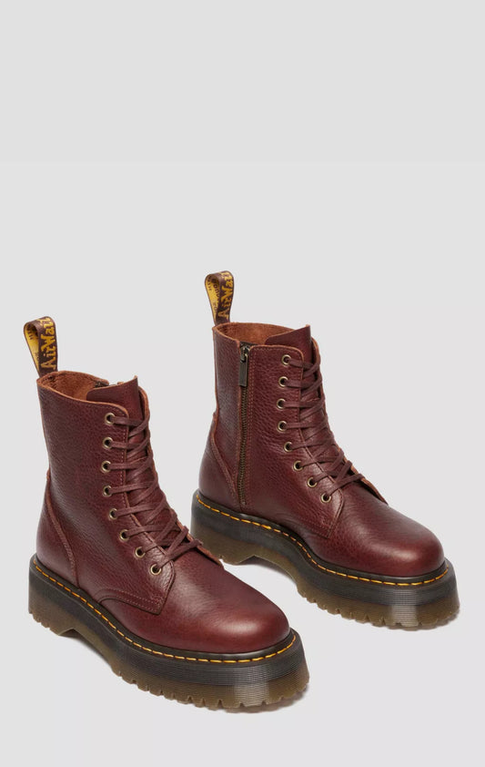 Pair of red leather boots with black soles on a light gray background