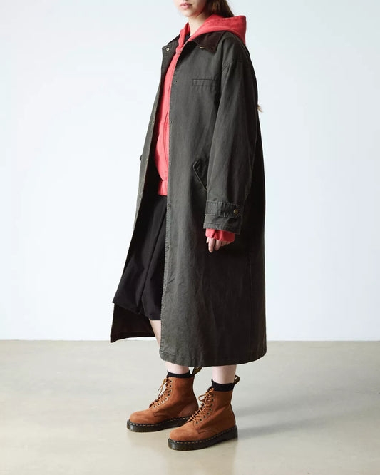 Person wearing a long dark coat over a red shirt with brown boots on a light background