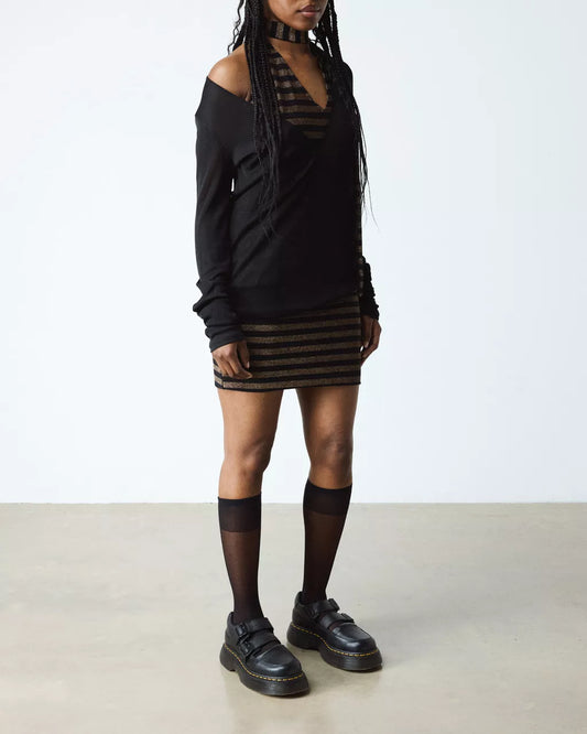 Person wearing a black outfit with a striped skirt on a plain background