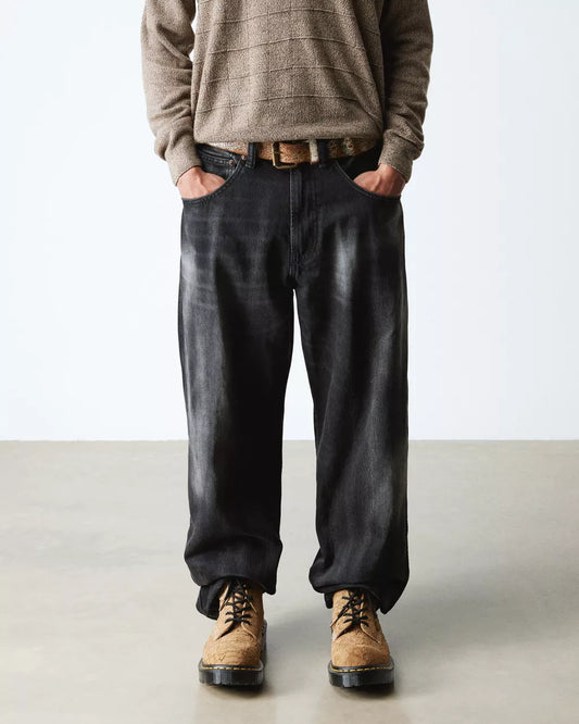 Person wearing a brown sweater, black pants, and tan boots on a plain background