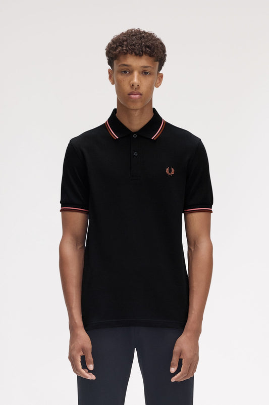 A man wearing a brown Fred Perry twin tipped polo shirt with white trim on the collar and sleeves, paired with white pants.