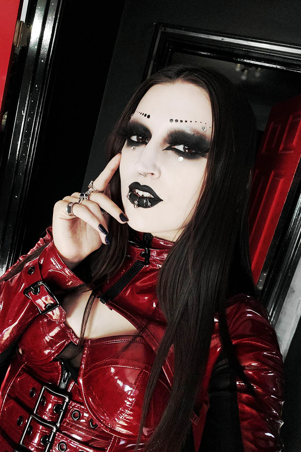 Person wearing a lip service red leather outfit with dark makeup, sitting inside a vehicle.