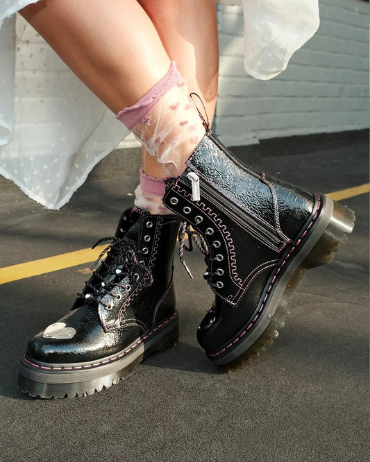 Black leather boots with glossy finish worn by a person on a concrete surface.