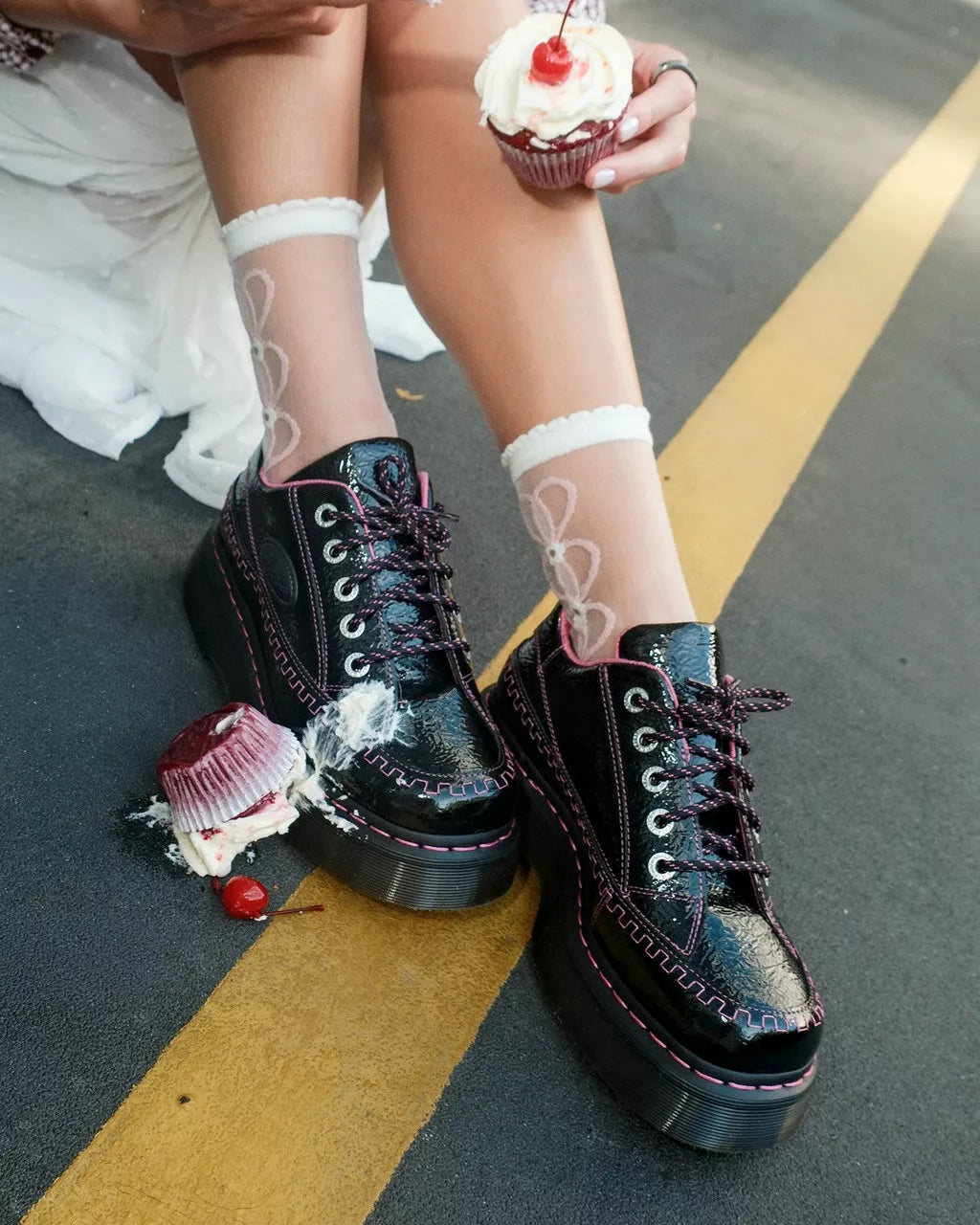 Black platform shoes with decorative elements worn by a person holding a cupcake.