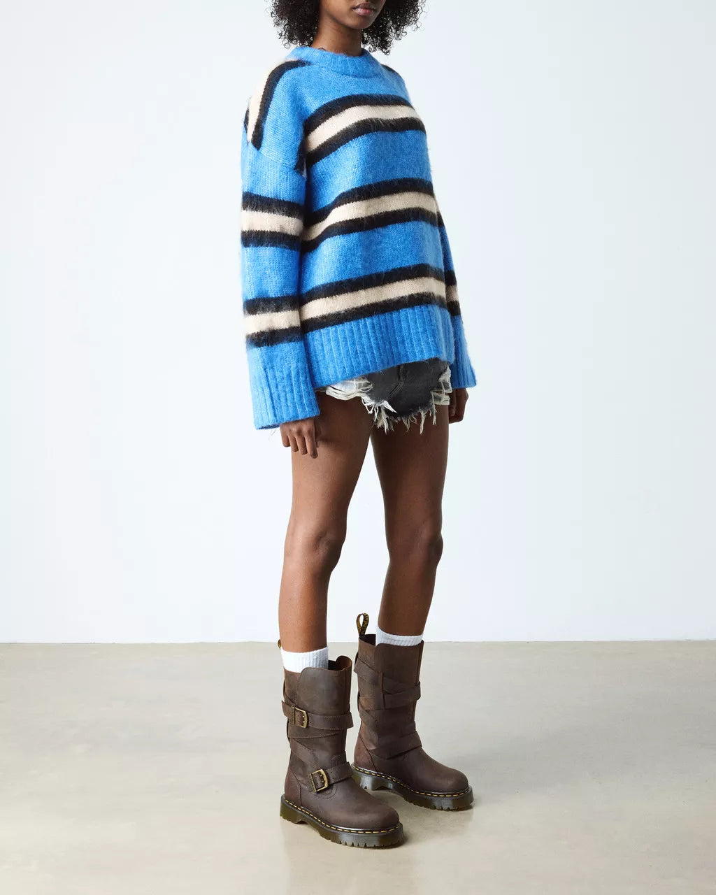 Person wearing a blue and white striped sweater with brown boots on a plain background