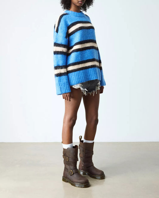 Person wearing a blue and white striped sweater with brown boots on a plain background