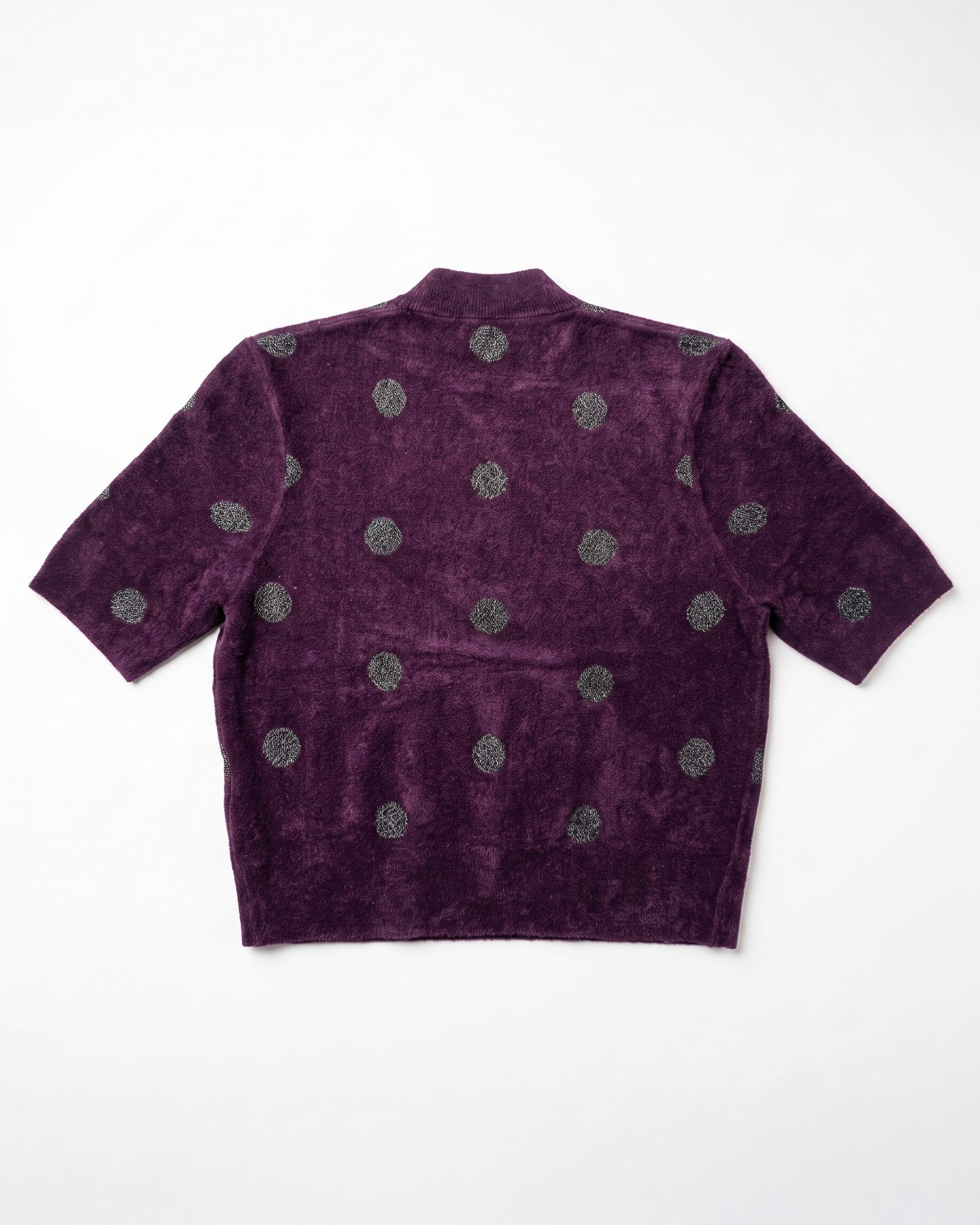 A short-sleeve cropped knit top in deep purple with a textured, velour-like finish, featuring a pattern of metallic silver-gray circular medallions, shown flat against a white background.