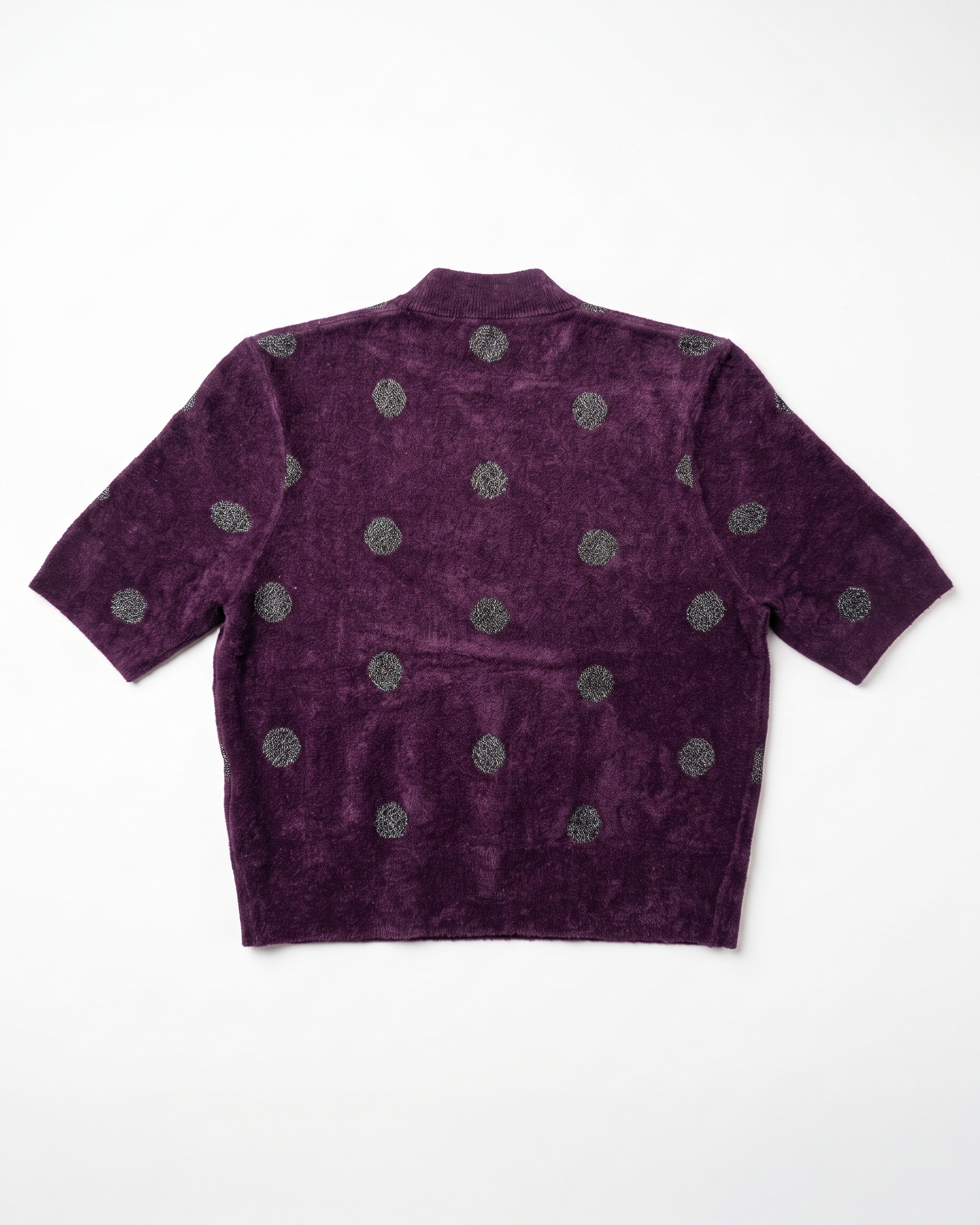 A short-sleeve cropped knit top in deep purple with a textured, velour-like finish, featuring a pattern of metallic silver-gray circular medallions, shown flat against a white background.