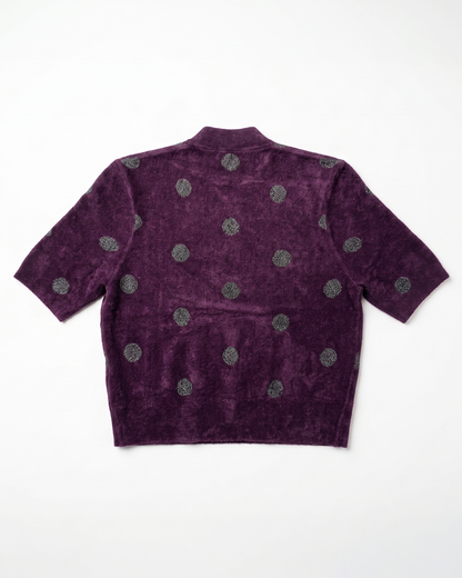 A short-sleeve cropped knit top in deep purple with a textured, velour-like finish, featuring a pattern of metallic silver-gray circular medallions, shown flat against a white background.