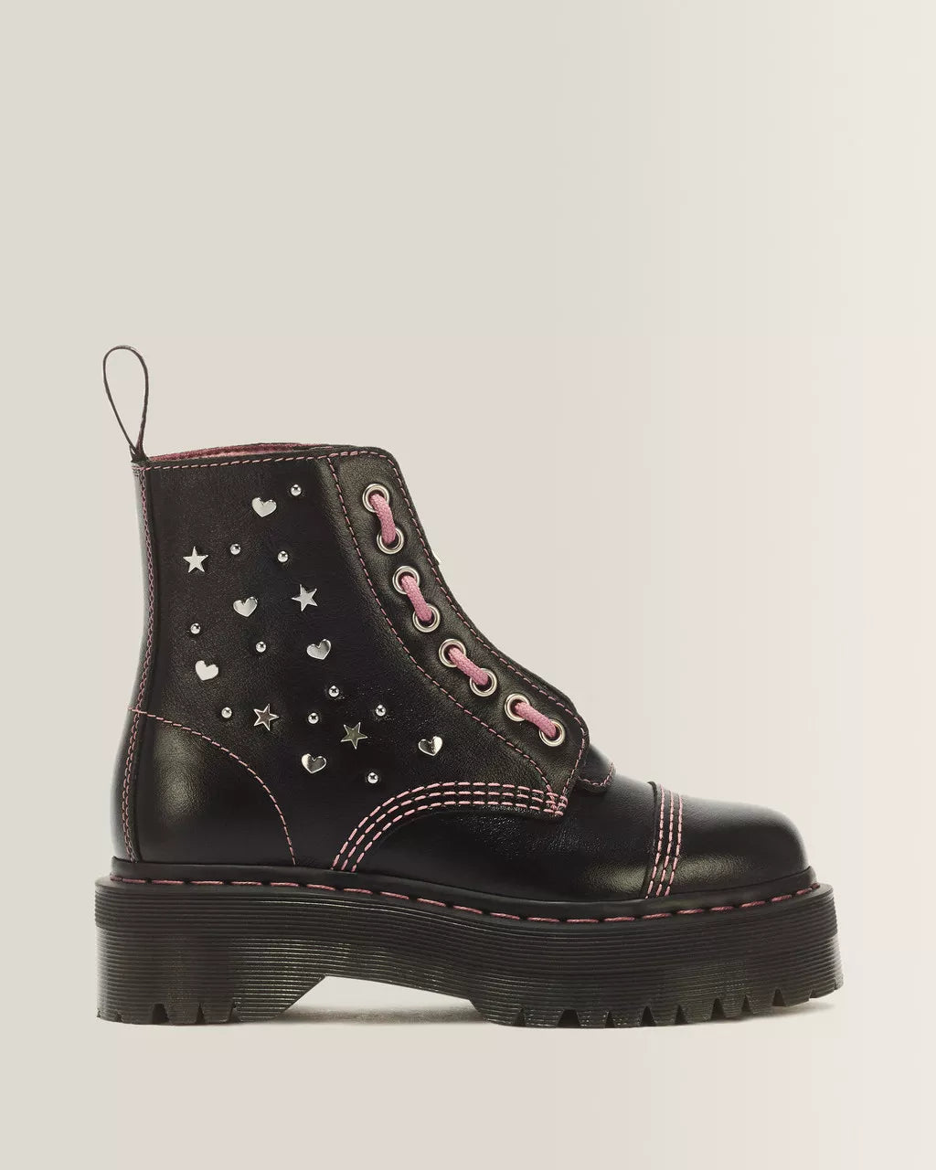 A black leather ankle boot with silver heart and star studs, pink laces, and pink contrast stitching, shown from a side profile on a light gray background.