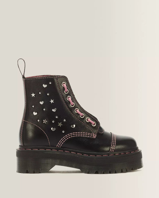 A black leather ankle boot with silver heart and star studs, pink laces, and pink contrast stitching, shown from a side profile on a light gray background.