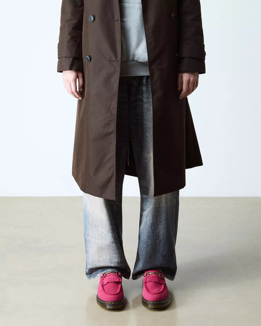 Person wearing a long brown coat, gray pants, and pink shoes on a light background