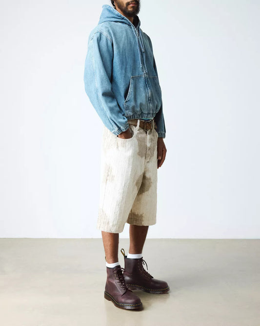 Person wearing a blue denim jacket, beige shorts, and brown boots on a white background
