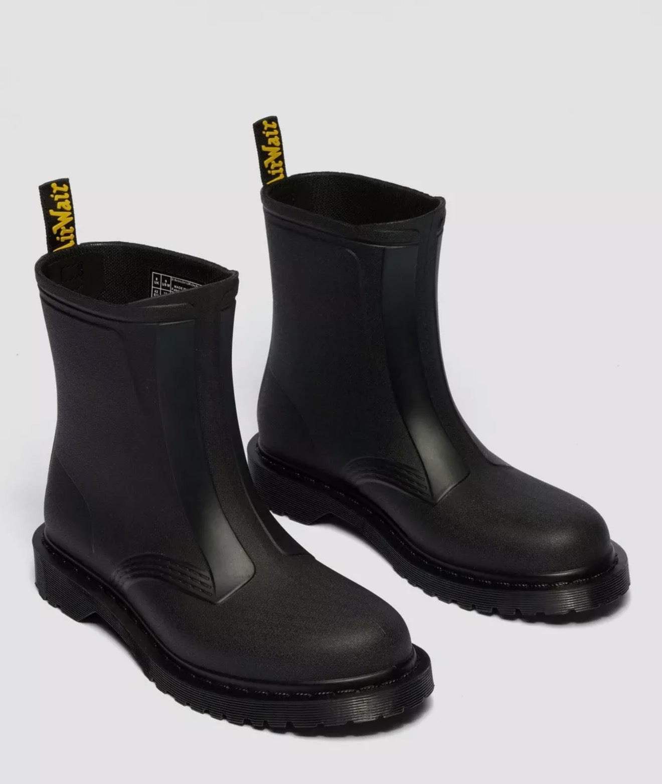 Pair of black rubber boots with yellow labels on a light gray background