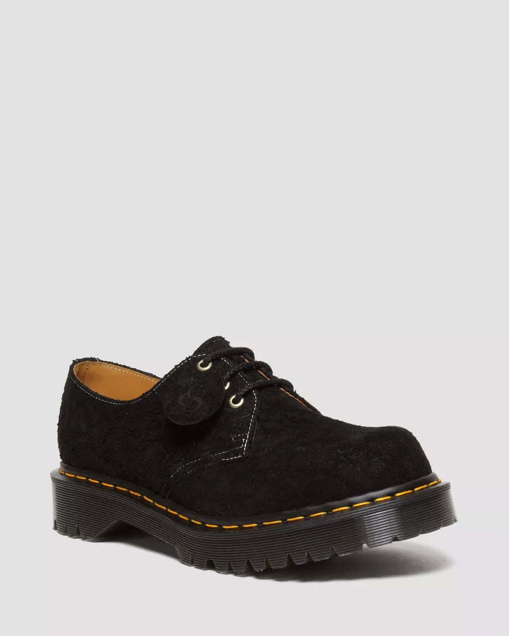 Black leather shoe with yellow stitching on a light gray background
