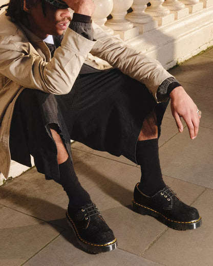 Person wearing black Dr. Martens shoes sitting on a stone floor.