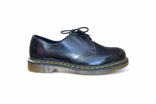 Shiny black shoe with yellow stitching on a white background