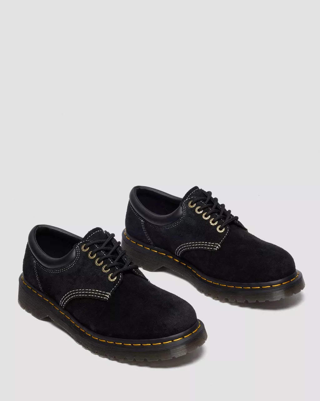 Pair of black suede shoes with yellow stitching on a light gray background