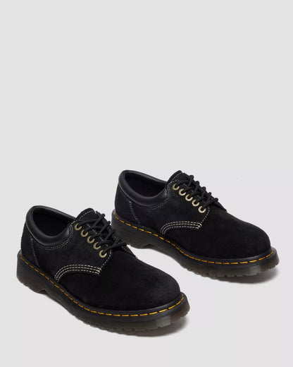 Pair of black suede shoes with yellow stitching on a light gray background