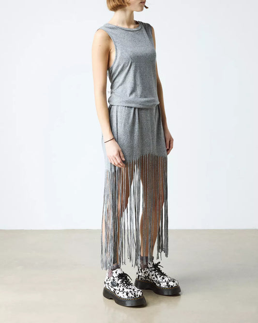 Person wearing a gray sleeveless top and fringe skirt with black and white shoes on a plain background