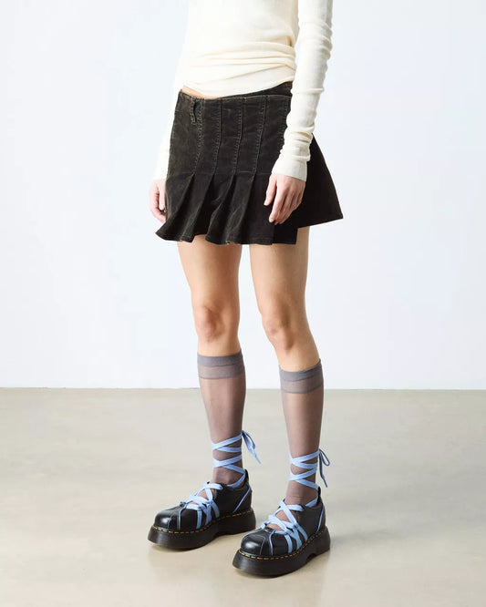 Person wearing a black pleated skirt, white long-sleeve top, gray knee-high socks with blue accents, and black platform shoes on a light background.