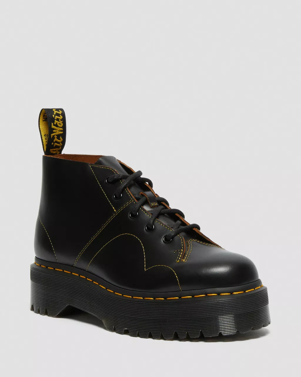 Black leather boot with yellow stitching on a light gray background