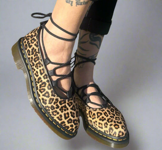 A pair of leopard print flat shoes with laces, on a person's feet.