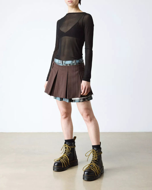 Person wearing a black sheer top, plaid skirt, and black boots on a plain background