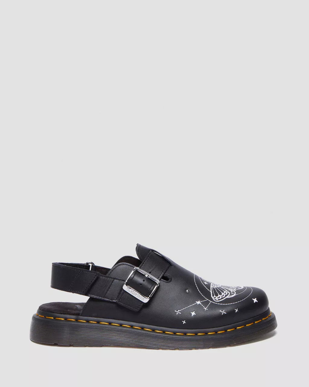 A black leather mule with embroidered moth and star motifs, featuring a silver buckle.