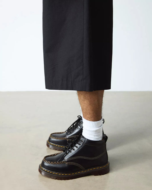 Person wearing black leather boots with white socks on a neutral background