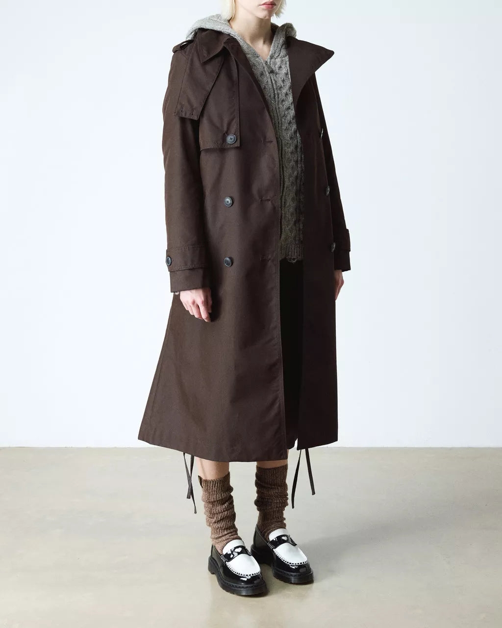 Person wearing a long brown coat with a white background