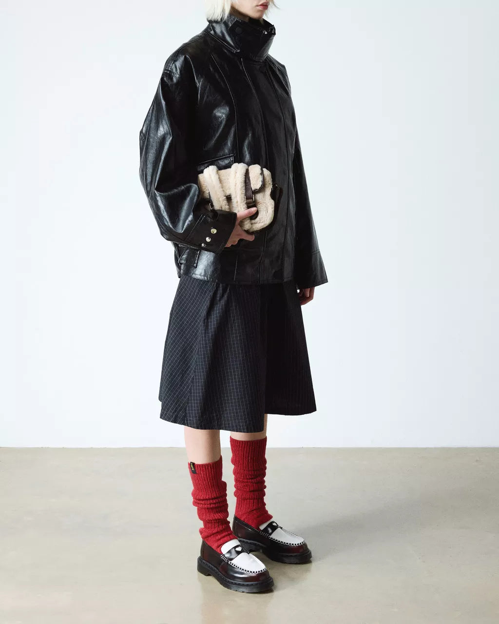 Person wearing a black coat, skirt, and red socks with white shoes on a plain background