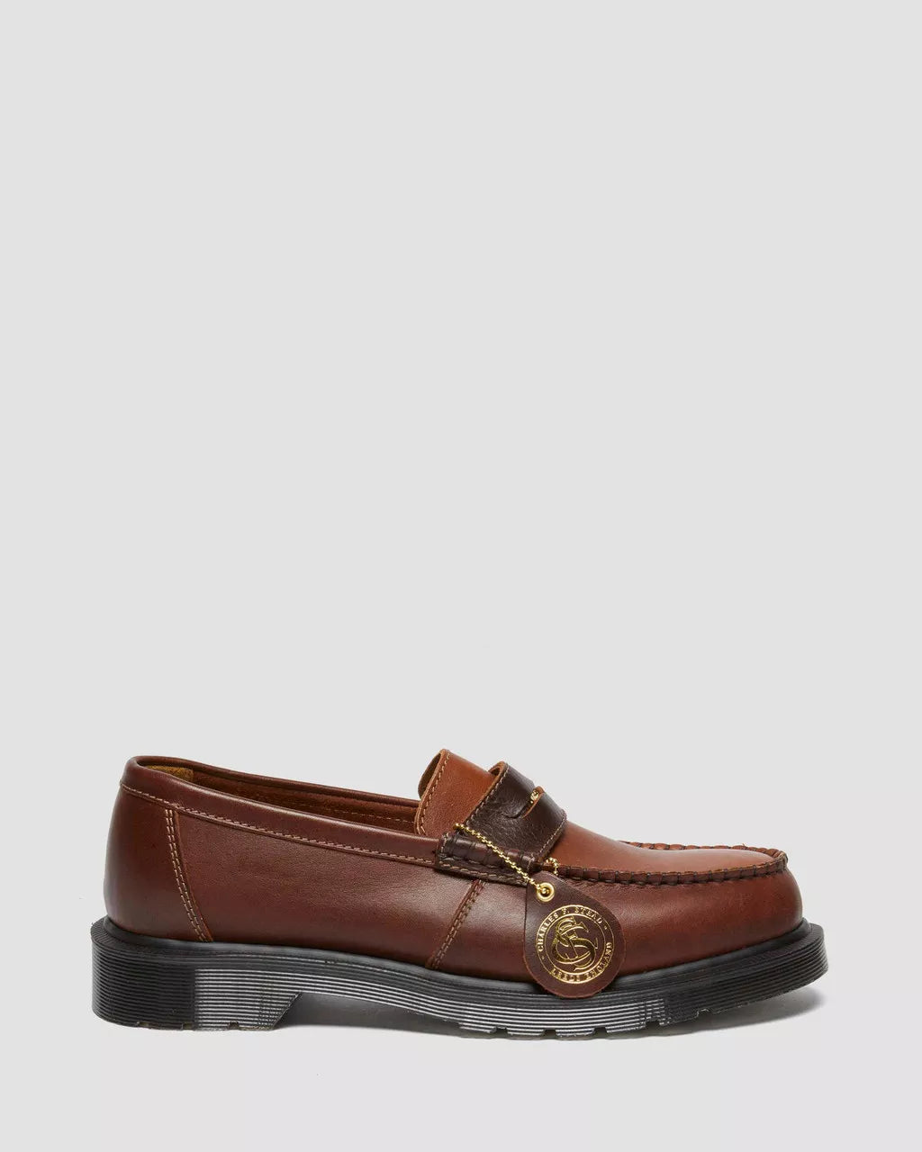 A brown leather loafer with a gold penny strap and black welt stitch on a white background.