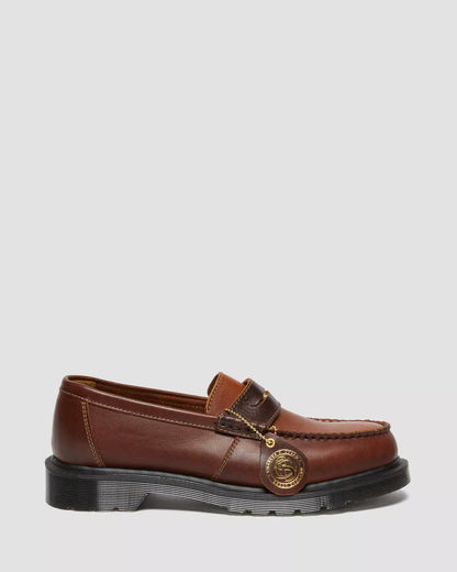 A brown leather loafer with a gold penny strap and black welt stitch on a white background.