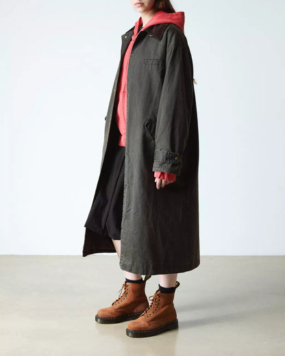 Person wearing a long dark coat over a red shirt with brown boots on a light background