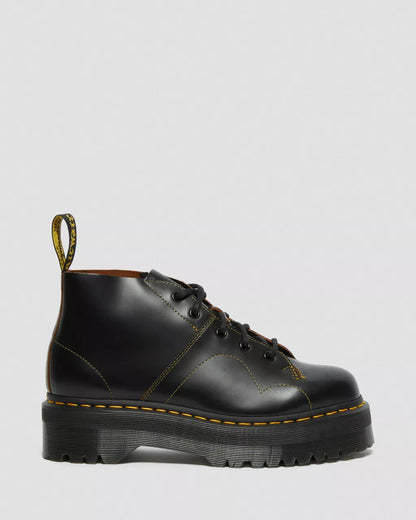 Black leather boot with yellow stitching on a light gray background