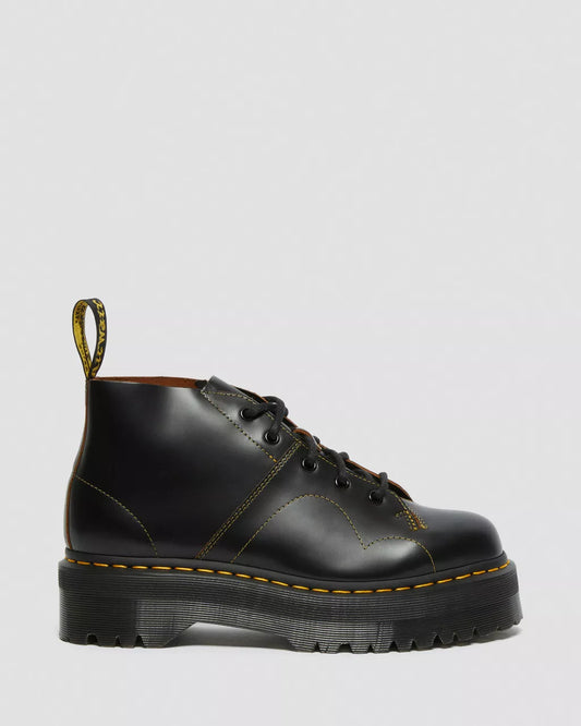 Black leather boot with yellow stitching on a light gray background