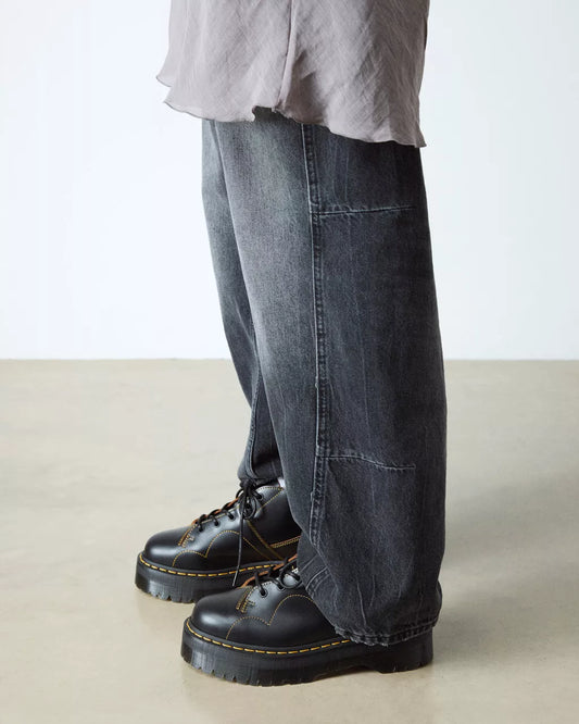 Person wearing dark blue jeans and black boots on a plain background