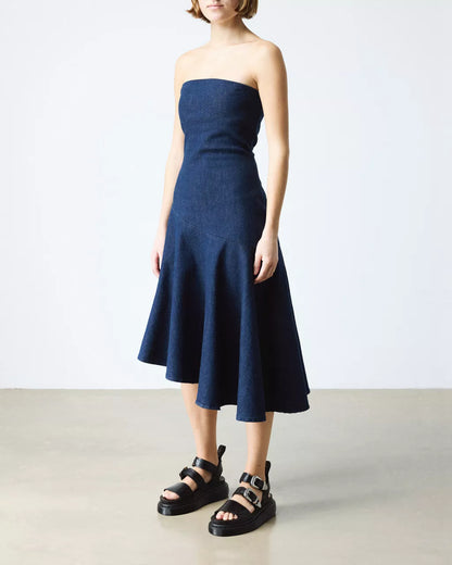 Woman wearing a strapless navy dress with black sandals on a white background