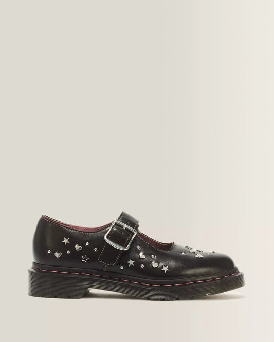 A single black leather Mary Jane shoe decorated with silver metal studs in the shape of stars and hearts, featuring a hook-and-loop strap with a silver buckle, set against a light gray background.