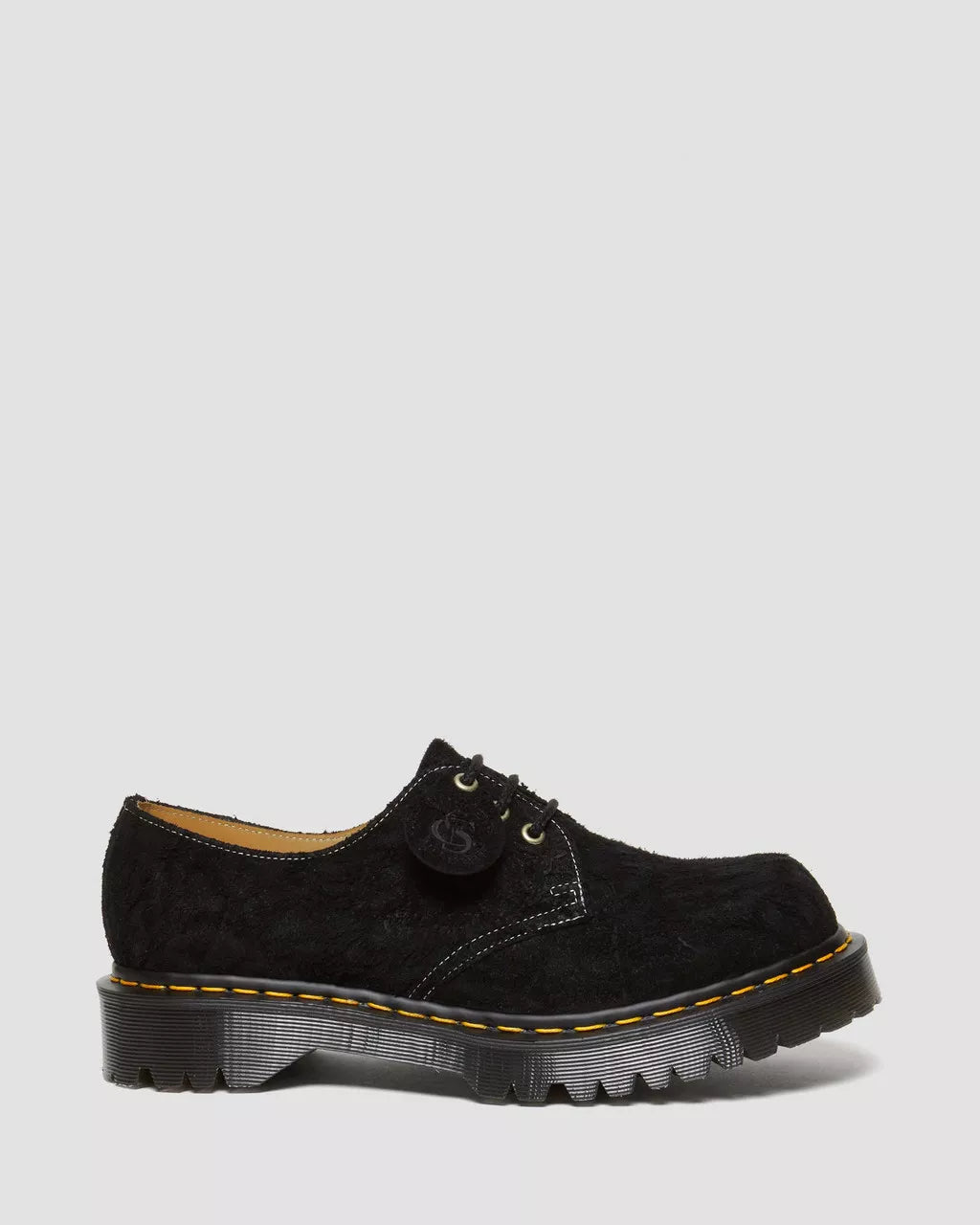 Black suede shoe with yellow stitching on a light gray background