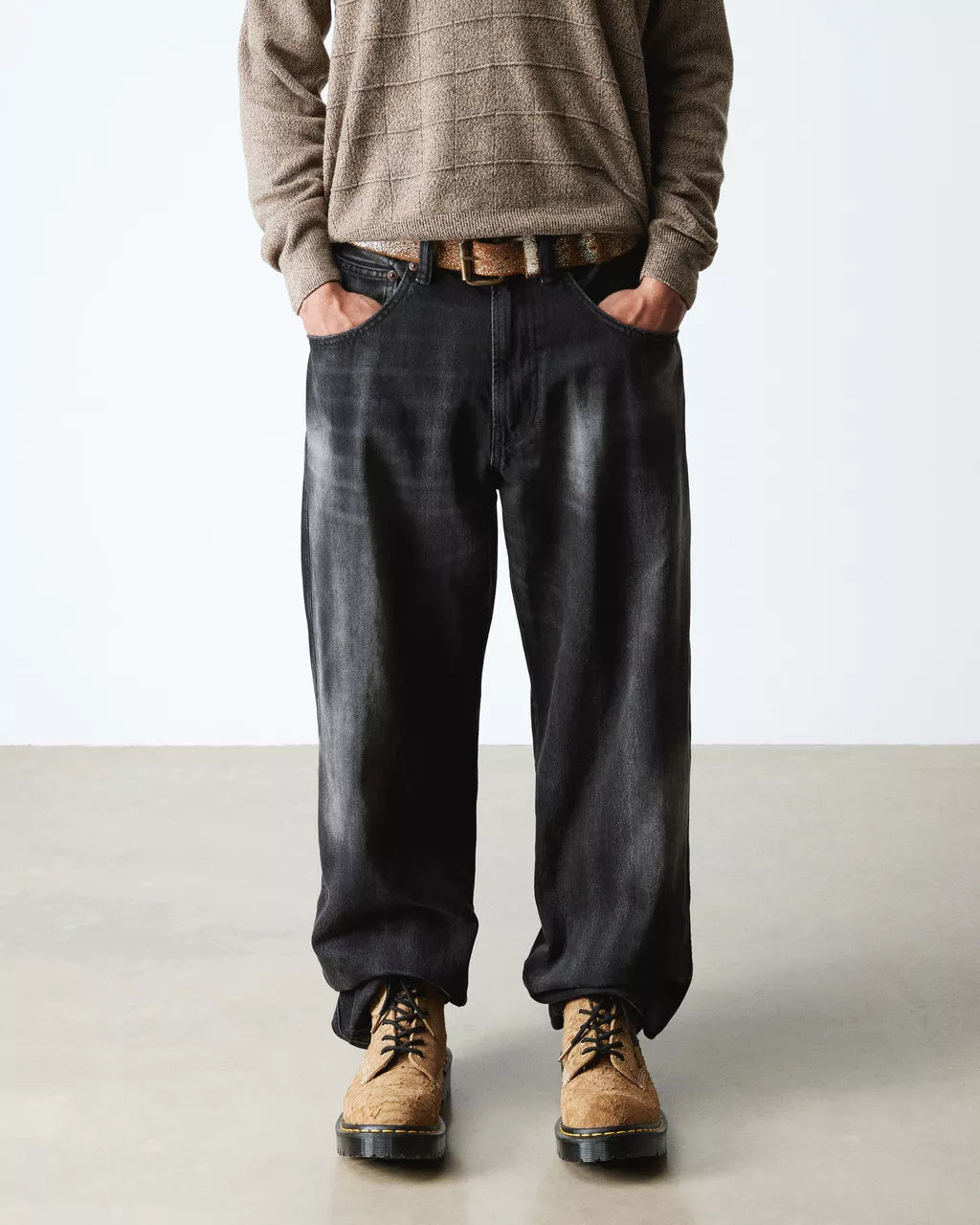 Person wearing a brown sweater, black pants, and tan boots on a plain background