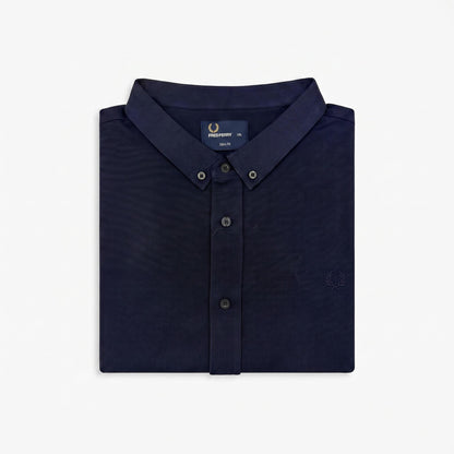 A folded navy blue button-down shirt by Fred Perry, shown on a clean white background. The shirt features a classic collar, button-down front, and the signature embroidered laurel wreath logo on the chest.