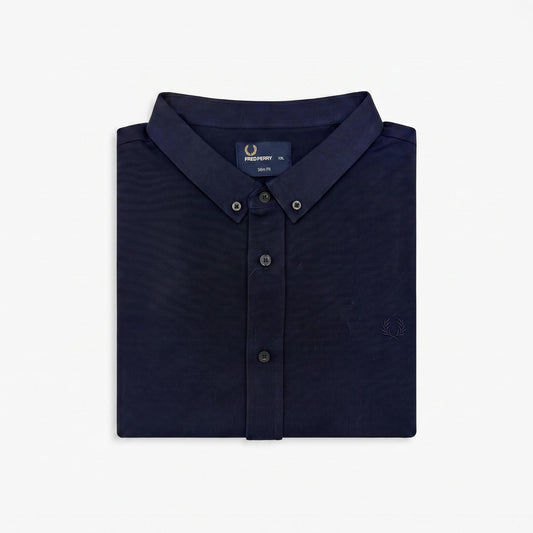 A folded navy blue button-down shirt by Fred Perry, shown on a clean white background. The shirt features a classic collar, button-down front, and the signature embroidered laurel wreath logo on the chest.