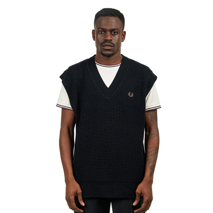 Man wearing a black sleeveless vest over a white shirt on a white background