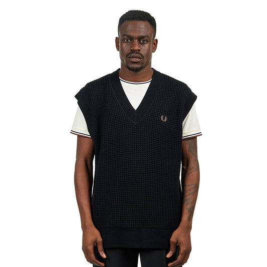 Man wearing a black sleeveless vest over a white shirt on a white background