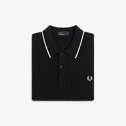A folded black ribbed knit polo shirt by Fred Perry, featuring white piping along the collar and a small embroidered white logo on the chest, set against a plain white background.
