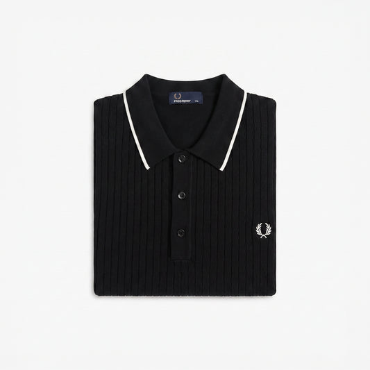 A folded black ribbed knit polo shirt by Fred Perry, featuring white piping along the collar and a small embroidered white logo on the chest, set against a plain white background.