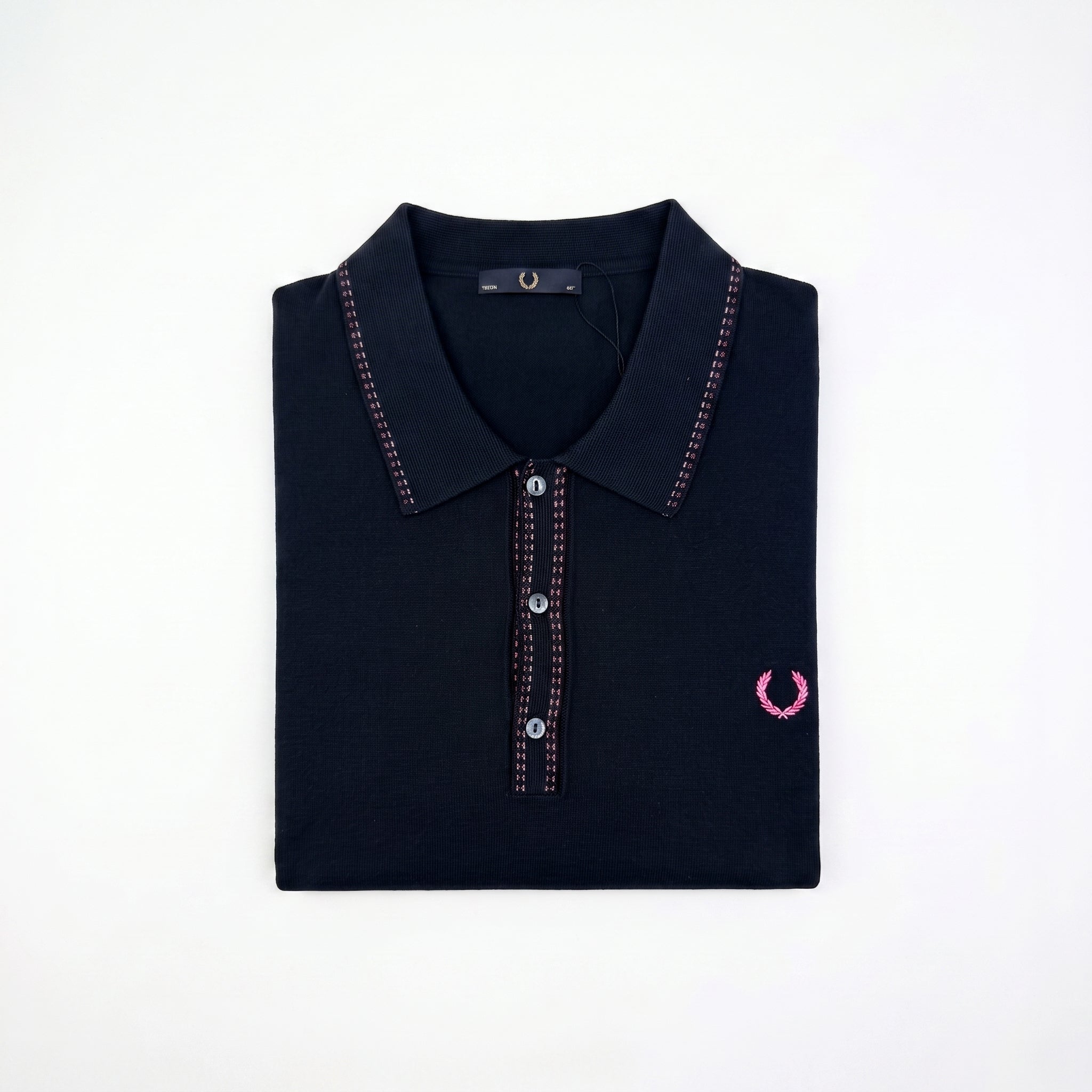 A folded dark navy polo shirt with pink contrast stitching and a pink embroidered laurel wreath logo on the left chest, displayed on a clean white background.